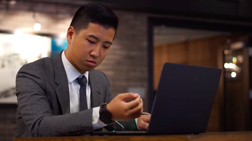 A person in front of a computer looks at the wristband of his smartwatch