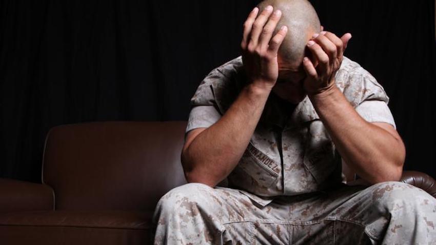 A soldier in uniform sits with his head in his hands.